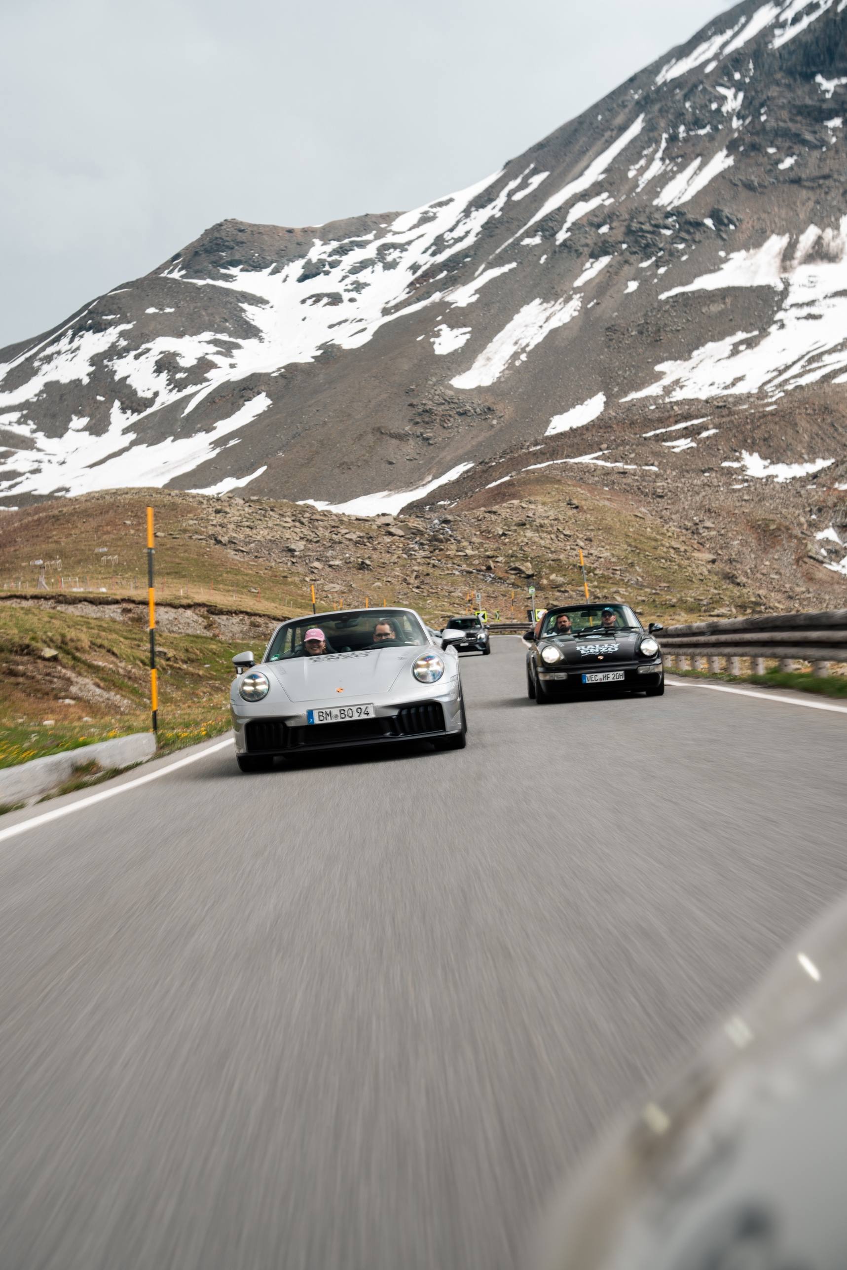 Zwei Porsche 911 Cabriolets auf einer Hochgebirgsstraße zwischen Schneefeldern