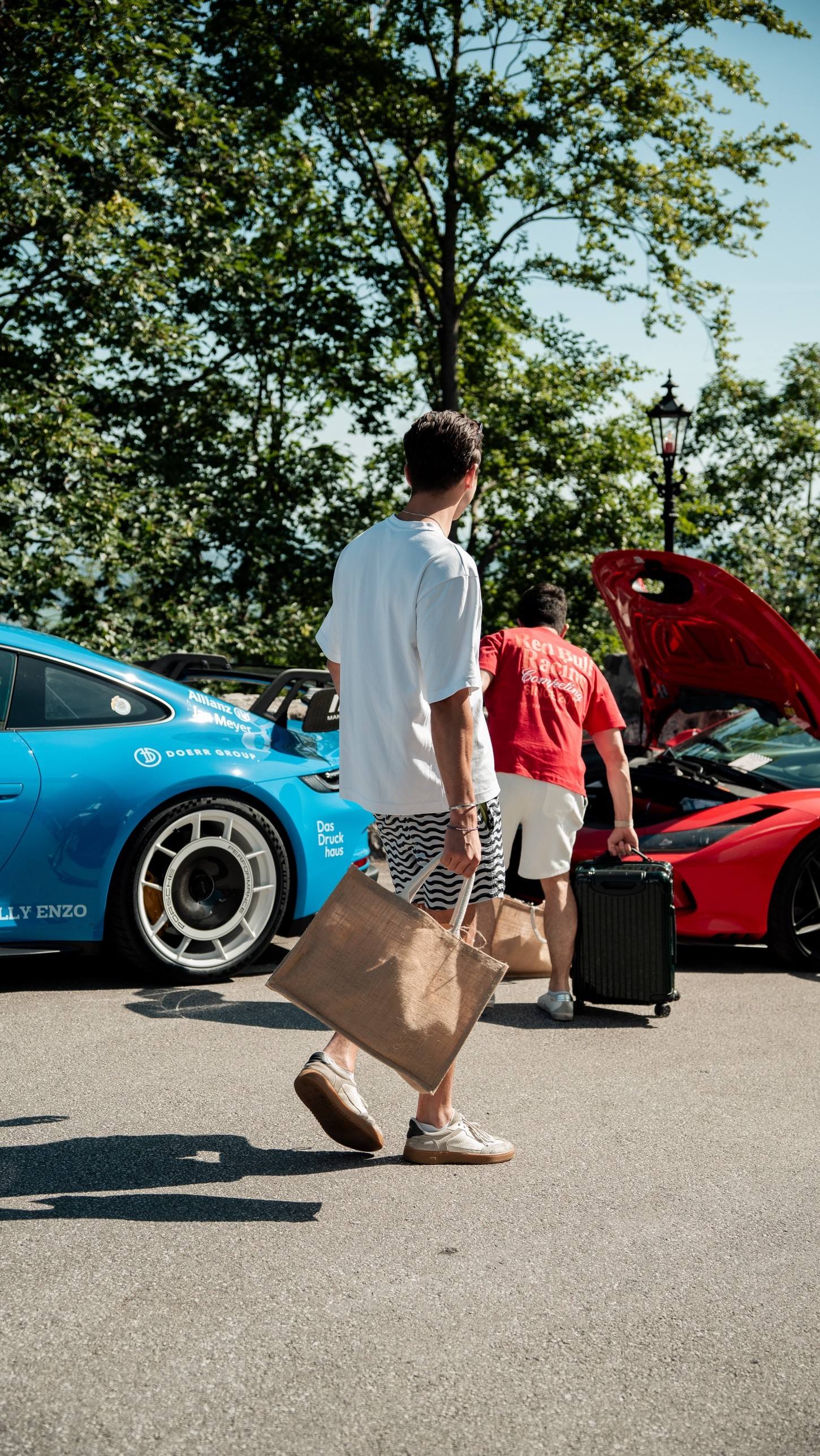 Teilnehmer mit Jutetasche geht zu blauem Porsche und rotem Ferrari mit offener Haube