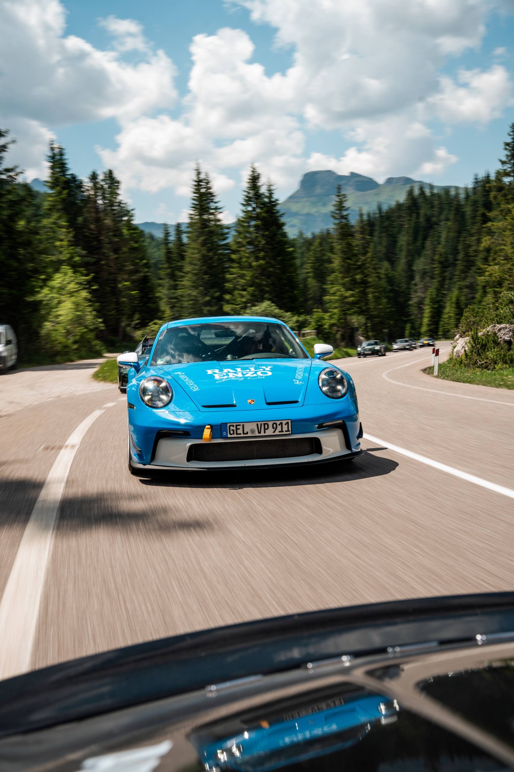 Blauer GT3 mit RALLY-ENZO-Beklebung in einer Kurve, aus dem vorausfahrenden Wagen fotografiert