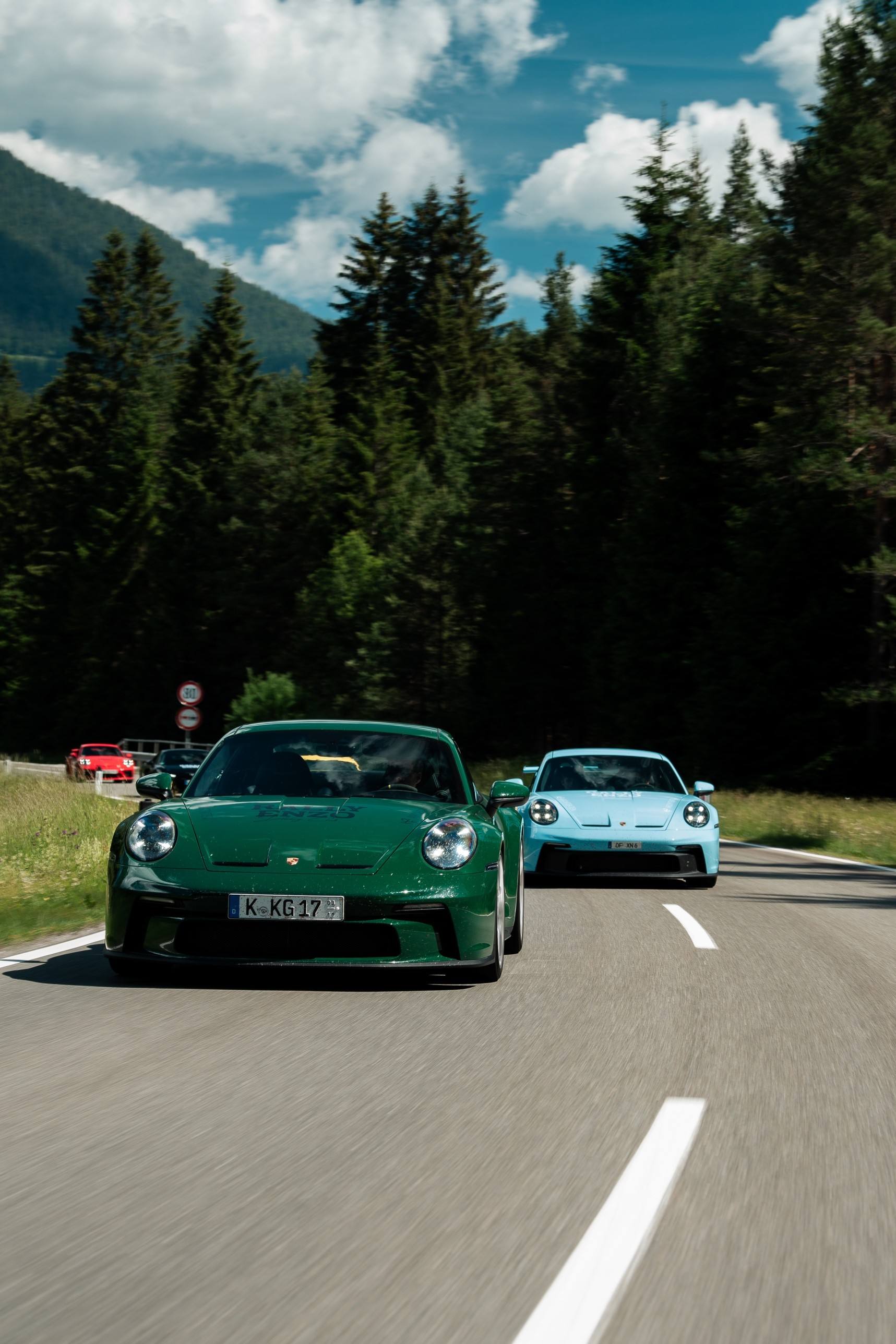 Grüner und hellblauer Porsche GT3 auf einer Landstraße zwischen Fichtenwäldern
