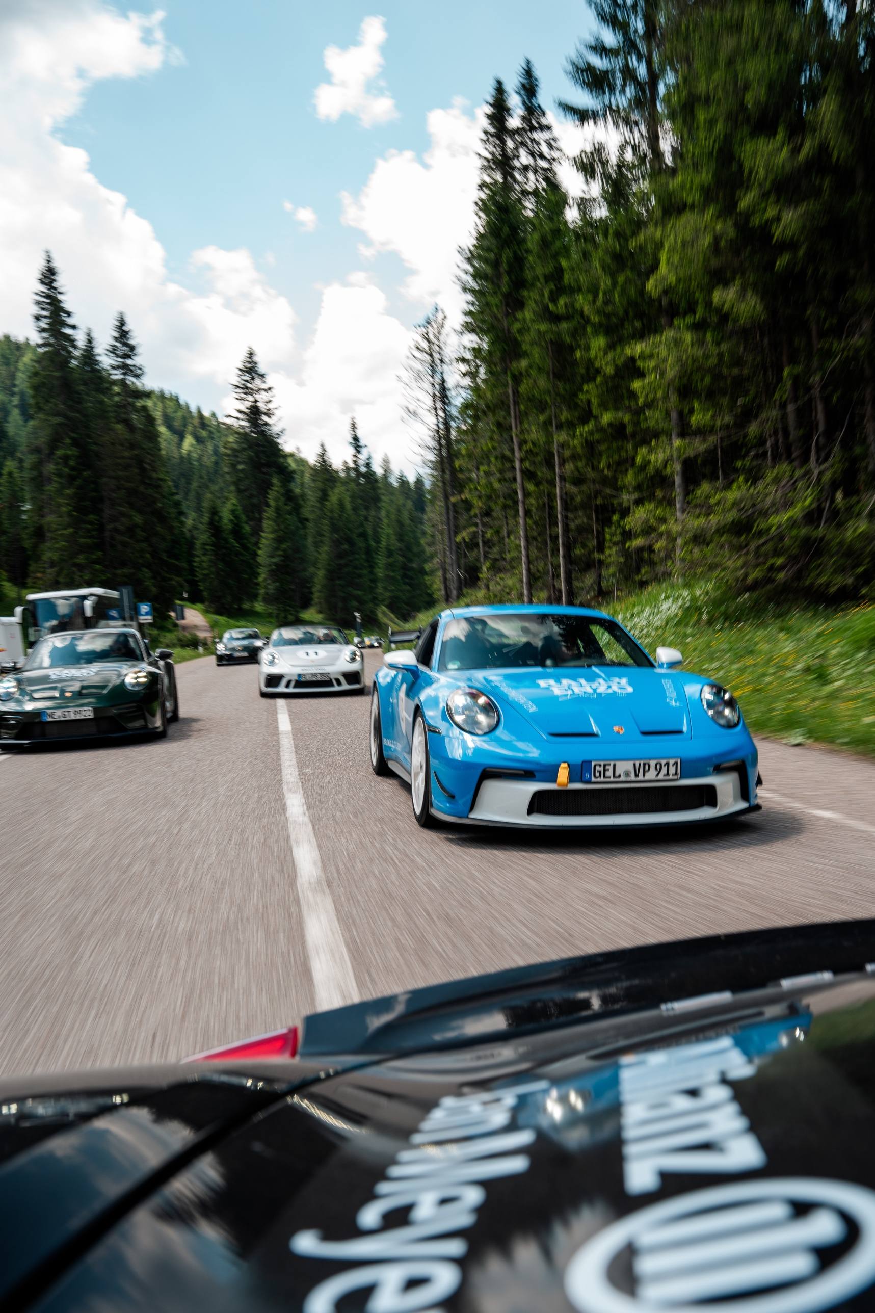 Kolonne aus Sportwagen mit blauem GT3 vorn auf einer Waldstraße