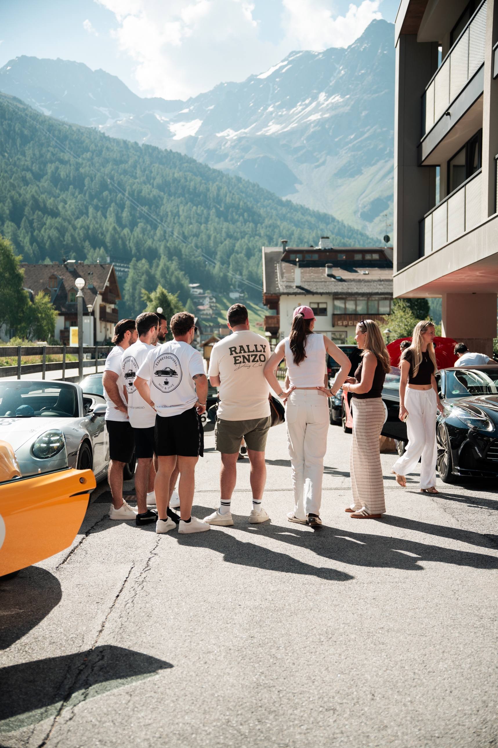 Teilnehmer und Sportwagen vor einem Hotel in einem Gebirgstal