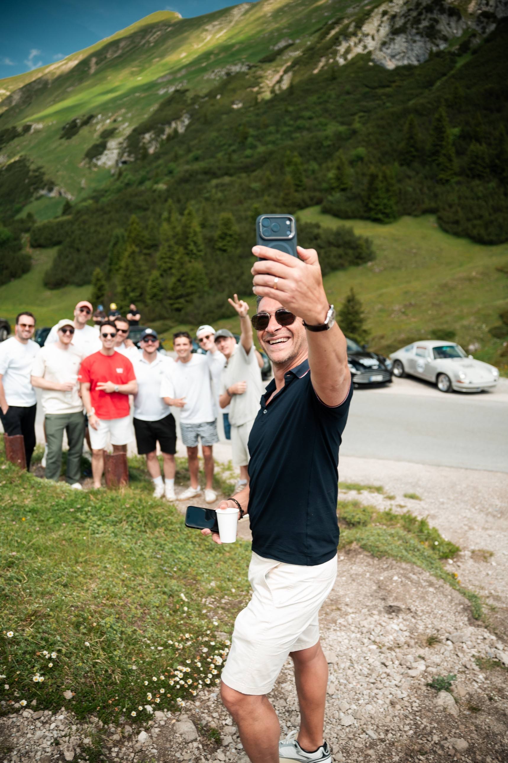 Gruppen-Selfie der Teilnehmer an einer Passhöhe, dahinter ein klassischer Porsche